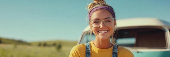 Young woman with glasses and a headband smiles in front of a vintage van on a sunny day photo