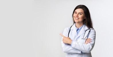 Smiling Doctor Lady Pointing Finger At Copy Space Standing Over Gray Background. Studio Shot, Panorama photo