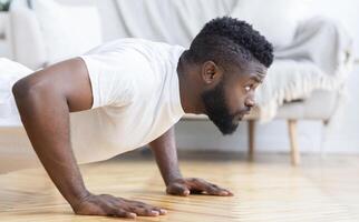 Young black man exercising in his house gym, doing push ups, side view, free space photo