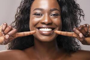 Teeth alignment and whitening concept. Happy african american girl pointing at her wide smile with two forefingers over grey background, closeup photo