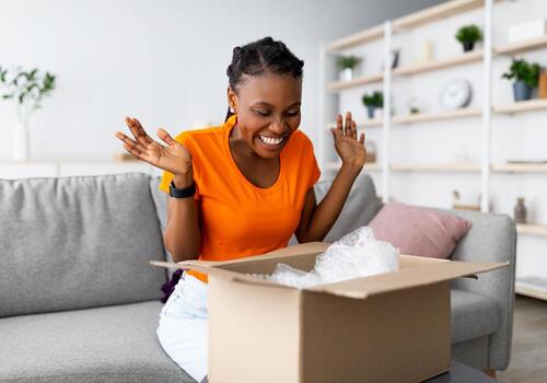 lleno de alegría afro mujer desembalaje caja de cartón parcela, emocional acerca de exitoso compras, satisfecho con genial compra a hogar. en línea almacenar, de confianza entrega Servicio concepto foto