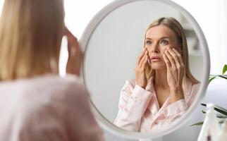 Skin Problems Concept. Upset Middle Aged Woman Looking At Mirror And Touching Face, Confused Mature Lady Noticed Wrinkles And Dark Circles Under Eyes, Unhappy With Skincare Routine, Selective Focus photo