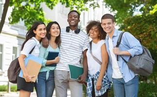 Group of international students posing in front of university, looking at camera and smiling photo