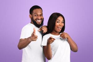 Portrait Of Excited African American Young Couple Pointing Fingers At Camera, Happy Man And Woman Choosing You, Having Fun, Standing Isolated Over Blue Studio Background, Copy Space photo