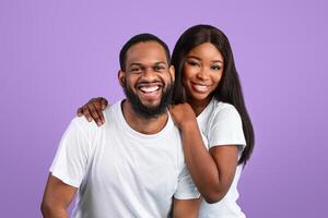 Love And Care. Portrait of charming millennial black woman embracing her man, couple in casual white t-shirts standing isolated over blue studio background wall, posing and looking at camera photo