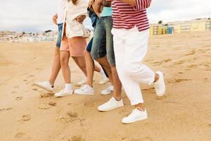 A group of friends stroll together along the sandy beach, their feet leaving footprints in the soft sand. The sun sets behind them, creating a warm, relaxed atmosphere on the shoreline. photo
