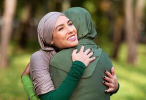 Two Multiracial Islamic Ladies Hugging Posing Standing Outdoors In Green Park. Happy Islamic Females Embracing Expressing Their Love And Support. Unity And Friendship Concept photo
