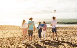 A group of five friends stands on the sandy beach, enjoying a sunny day. They are playing with a ball and laughing as the waves crash gently behind them. photo