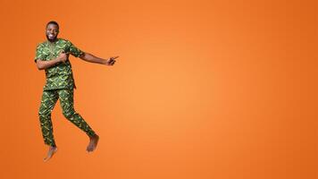 Excited black guy jumping up and pointing at free space, yellow studio background photo