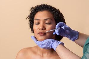 A woman with curly hair relaxes as a clinician administers injections to enhance her facial features in a well-lit medical office setting. The atmosphere feels calm and professional. photo