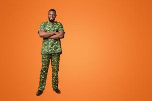 Smiling african american guy in authentic costume posing over yellow background, holding arms crossed photo