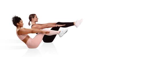 Two women are engaged in synchronized core exercises, sitting with legs raised and leaning back. The brightly lit gym offers a clean and modern atmosphere for workout routines. photo