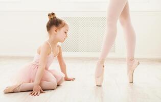 Little girl looking at professional ballet dancer. Cute baby dreaming to become ballerina, copy space. Classical dance school background, practicing for children, crop photo