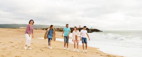 A family strolls along a sandy beach while enjoying the cool ocean breeze. They are casually dressed, laughing, and creating lasting memories near the water's edge on a cloudy day. photo