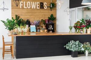 Small business. Modern flower shop interior, reception desk. Floral design studio, sale of decorations and arrangements. Flowers delivery service and sale of home plants in pots, wooden showcase. photo