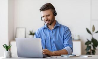 Handsome Young Man In Headset Study Online, Watching Webinar On Laptop, Enjoying Distance Education And Learning In Internet, Sitting At Desk At Home, Looking At Computer Screen, Free Space photo