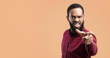 Hey, You. Portrait of angry african american guy pointing finger at camera, isolated over yellow studio background. Mad black man blaming and scolding someone behind camera, copy space photo