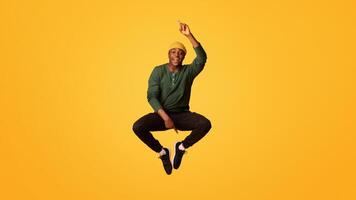 Check This. Cheerful Young Black Guy Pointing Up And Down While Jumping In Air, Positive Funny African American Hipster Man Demonstrating Free Copy Space On Yellow Background, Vertical Shot photo