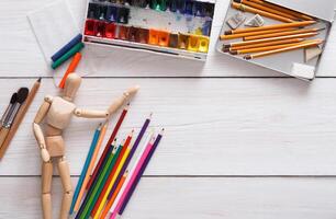 Workplace of artist, top view, copy space. Paints and wooden painter man with brushes on white desk, flat lay, objects photo