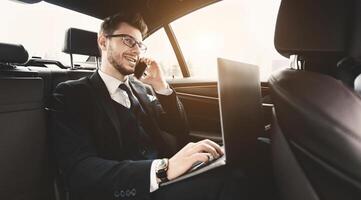 Always In Touch. Confident chief executive in suit using personal computer and making phone call in taxi, copy space, flare light photo