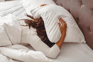 Loneliness. Depressed black woman lying alone in bed covering head with pillow feeling stressed afraid, suffering from insomnia, loud sounds of neighbors, has mental problems after divorcing husband photo