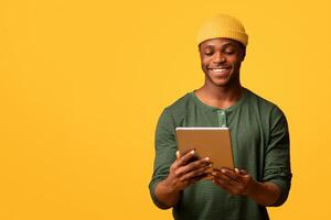 Portrait Of Young Smiling African American Guy Using Digital Tablet While Standing Over Yellow Studio Background, Cheerful Black Millennial Man Browsing New App Or Surfing Internet, Copy Space photo