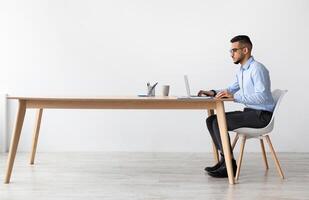Profile Side View Portrait Of Focused Middle Eastern Male Manager In Glasses Working On Laptop Computer In Modern Office, Serious Guy Sitting At Desk And Using Pc, Looking At Screen Watching Webinar photo