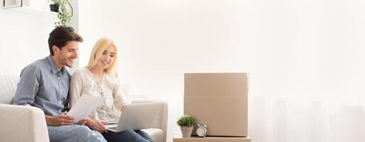Husband And Wife Using Laptop Looking Design Project Sitting On Couch In Own House. Moving Into New Home. Copy Space photo