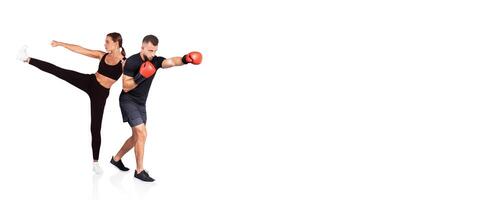 A woman performs a high kick while a man throws punches as part of a fitness routine. Both are dressed in athletic wear, showcasing their intense training session in a gym setting. photo