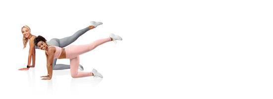 Two women are engaged in a fitness routine, showcasing leg lifts. They are in a bright, airy room, dressed in functional workout attire, focused on their exercise method. photo