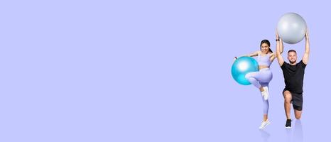 Two individuals are exercising indoors, one lifting a large silver exercise ball overhead while the other balances on one leg with a blue ball. They showcase motivation and strength. photo