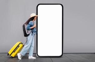 A traveler, wearing a hat and casual attire, stands beside a large, blank display at an airport terminal with a yellow suitcase, ready for departure and exploring new destinations. photo