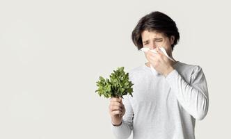 Portrait of unhealthy man with napkin blowing nose, looks to source of allergy photo