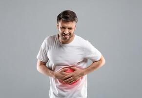 Middle-aged man holding his lightened with red right side, suffering from liver pain, grey studio background, copy space. Sad man having hepatitis, rubbing his right side. Liver diseases concept photo