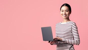 Portrait Of Young Smiling Asian Woman With Laptop Computer In Hands Standing Isolated Over Pink Background, Korean Female Working Online On Computer Or Browsing New Website, Panorama With Copy Space photo