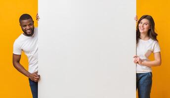 Big White Advertisement Board In Hands Of Happy Interracial Couple That Standing Over Yellow Background, Free Space For Your Text, Panorama photo