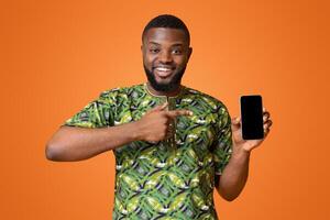 Happy african american man pointing at empty smartphone screen, recommending new application, yellow background photo