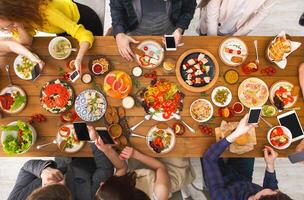 Online at dinner. Gadget device addiction, friends eating with smartphones, browsing in social networks while eating food together, table top view photo