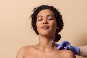 A woman sits calmly with her eyes closed while a professional administers a cosmetic injection to her neck. The peaceful environment reflects a sense of tranquility and care. photo