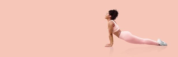 A woman performs a yoga pose in a minimalist pink studio. She focuses on her breath, engaged in a morning workout routine designed for flexibility and strength enhancement. photo