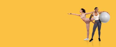 Two women practice fitness routines in a vibrant studio. One performs a balance stretch while the other holds a stability ball, showcasing different exercises for strength and flexibility. photo