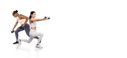 Two women are engaged in strength training exercises, each holding dumbbells. One is in a lunging position while the other completes a shoulder press. Bright lighting creates a motivated atmosphere. photo