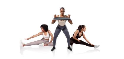 Three women participate in a fitness session, with one performing squats while holding a weight and the others stretching. The modern studio environment is bright and motivational. photo