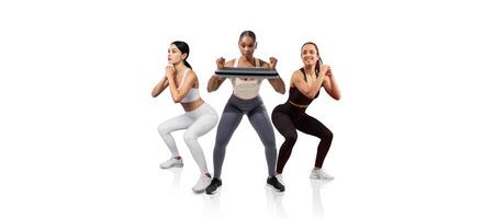 Three women are engaged in a workout routine, performing squats while holding weights. The bright, minimalist studio creates an energetic atmosphere for fitness activities. photo
