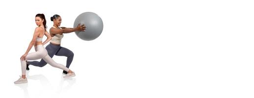 Two women are engaged in a fitness routine indoors. One is performing lunges while the other holds a stability ball, demonstrating strength and coordination during a workout session. photo
