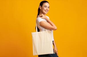 Stop Plastic Pollution. Woman Holding Blank White Eco Bag On Yellow Background In Studio. Free Space For Text photo