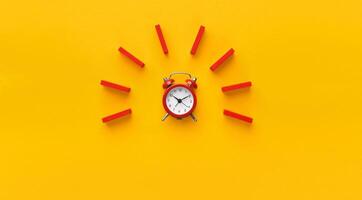 Alarm clock with red wooden dominoes on yellow background. Minimalism concept, panorama with empty space photo