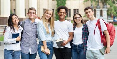 Diverse students in campus, posing in front of university and looking at camera photo