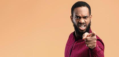 It's Your fault. Angry african american man pointing finger at camera, blaming you, yellow studio background photo