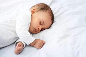 Beautiful Little Baby Boy Sleeping Peacefully Lying On Side In Bed Indoors, Resting During Daytime Sleep With Eyes Closed. Toddler Child Napping Indoors. High Angle, Cropped Shot With Copy Space photo